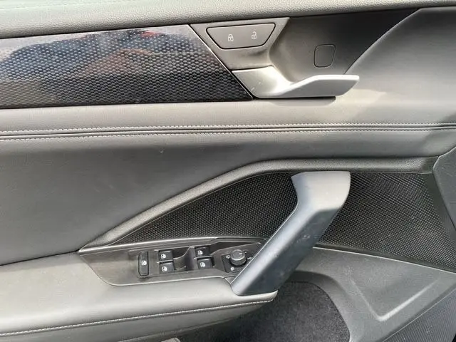 Détail de la porte intérieure côté conducteur du Volkswagen Tiguan 2024 noir, avec commandes électriques et poignée argentée.