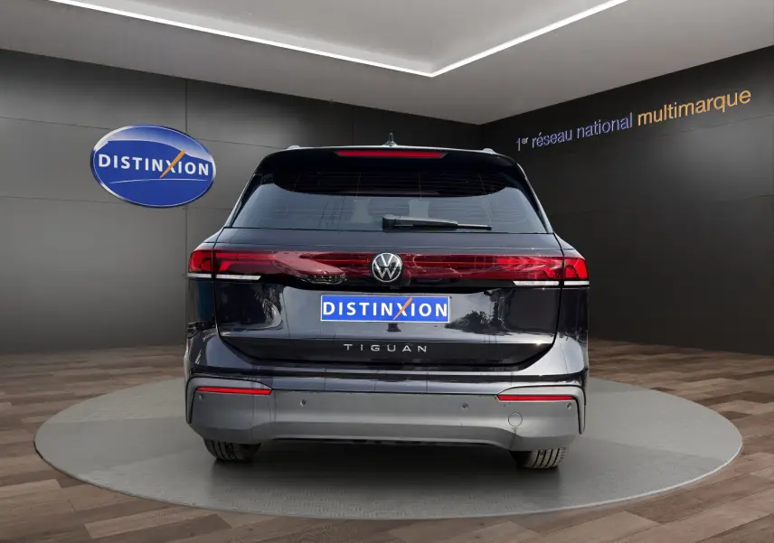 Vue arrière d'un Volkswagen Tiguan noir 2024 avec feux LED et logo distinctif sur fond showroom.