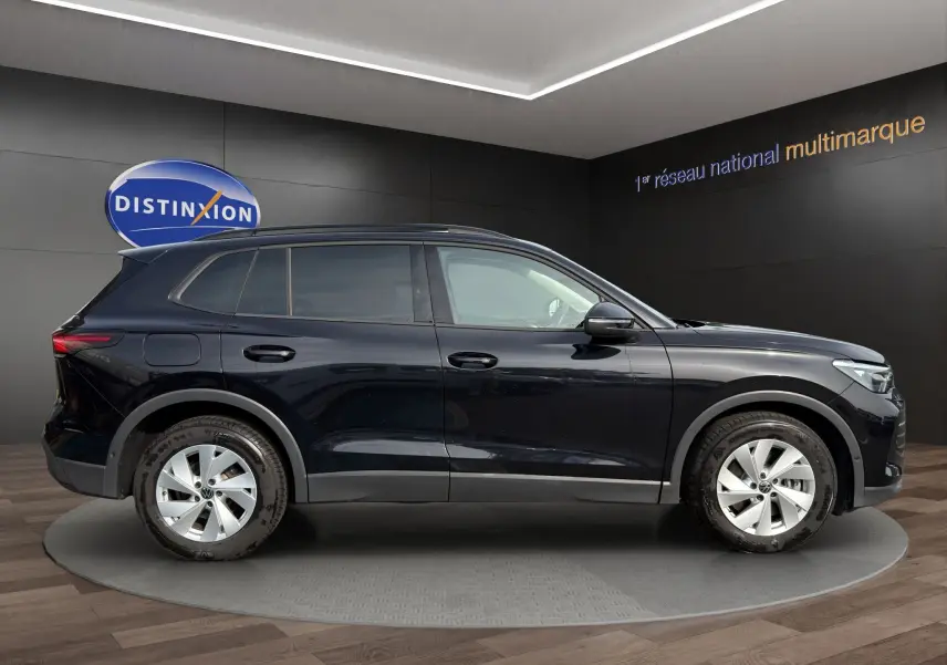 Vue de profil côté gauche d'un Volkswagen Tiguan noir 2024 dans un showroom avec jantes argentées.