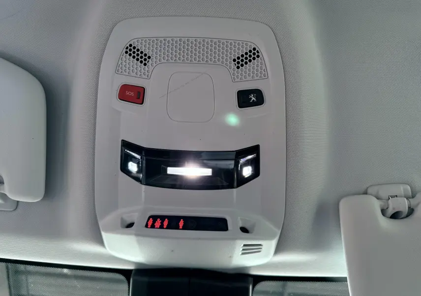 Vue en gros plan du plafonnier intérieur gris clair avec boutons SOS et logo Peugeot éclairés sur Peugeot 308 SW noir.