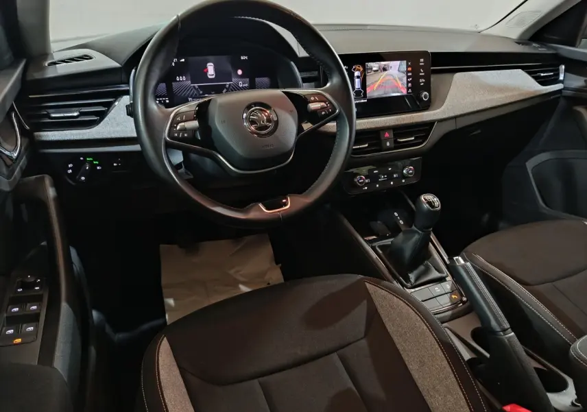 Intérieur avant du Skoda Kamiq 2024 gris clair, volant cuir multifonctions et écran tactile central avec caméra de recul.