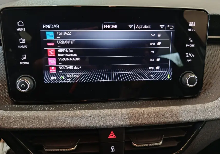 Écran tactile central du Skoda Kamiq 2024 affichant les stations radio FM/DAB, entouré de commandes noires.