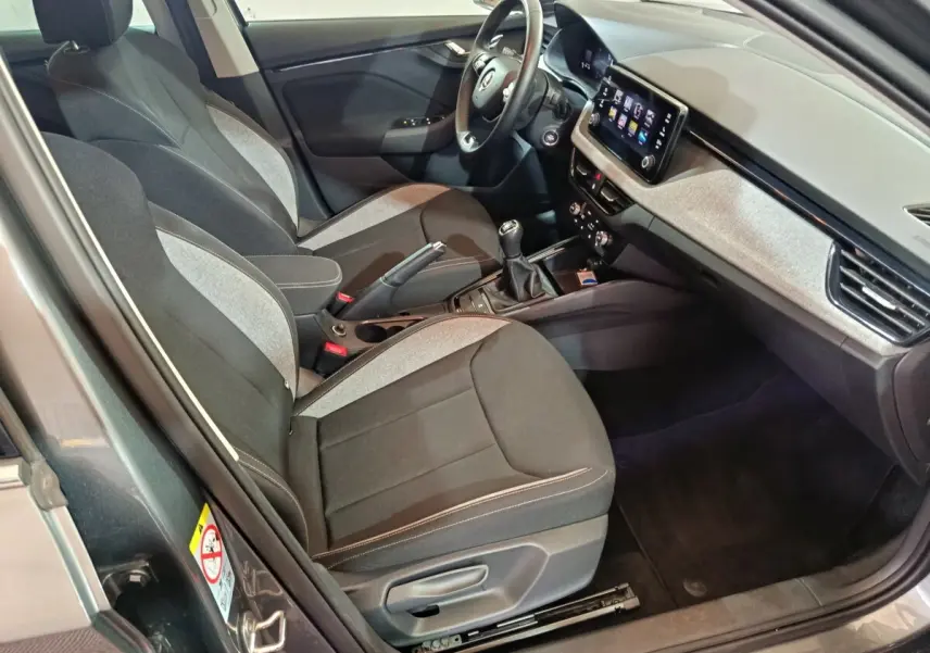 Vue intérieure côté conducteur de la Skoda Kamiq 2024 gris clair, volant cuir, écran tactile central et boîte manuelle.