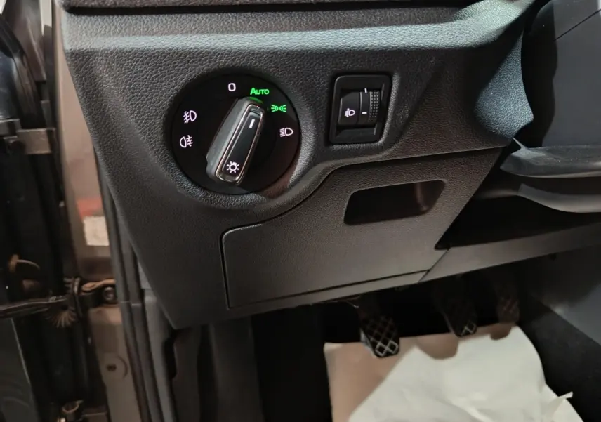 Gros plan sur le tableau de bord côté gauche du Skoda Kamiq gris clair 2024, montrant la commande des phares et réglage hauteur.