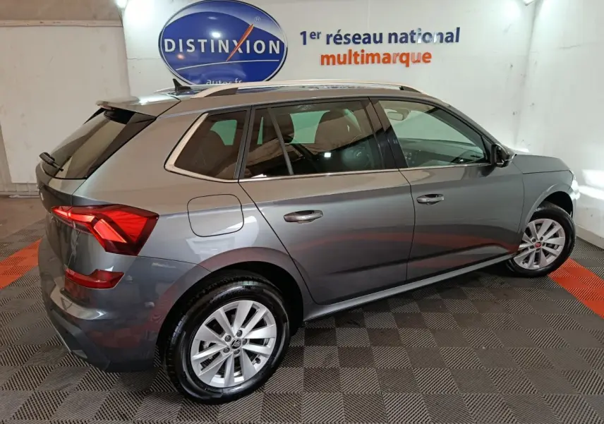Vue côté droit arrière d'un Skoda Kamiq gris clair 2024 dans un showroom avec éclairage intérieur.