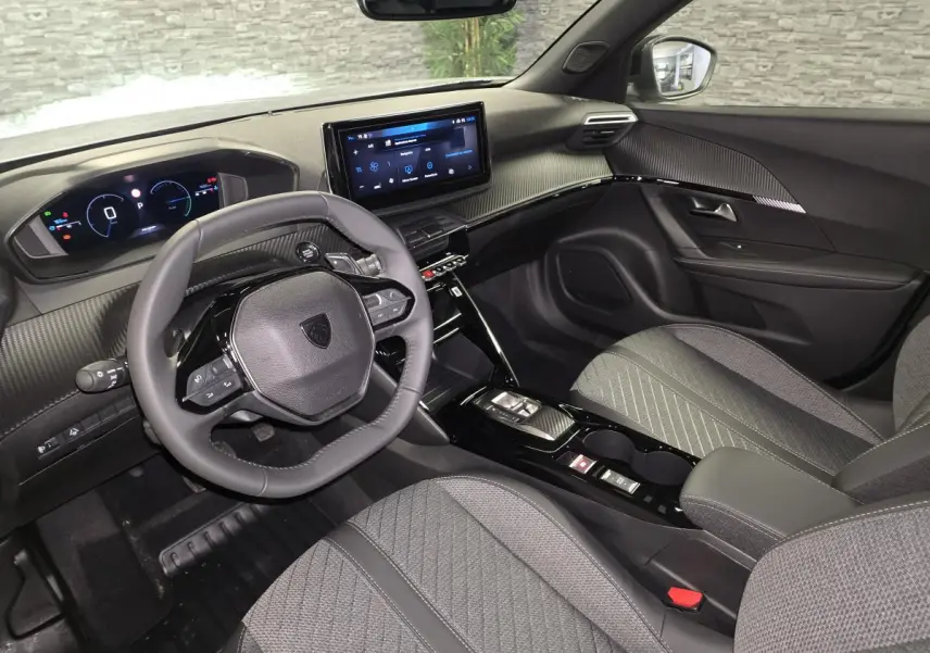 Vue intérieure avant droite du Peugeot 2008 1.2i Hybrid 2025, avec volant compact, tableau de bord numérique et sellerie tissu gris.