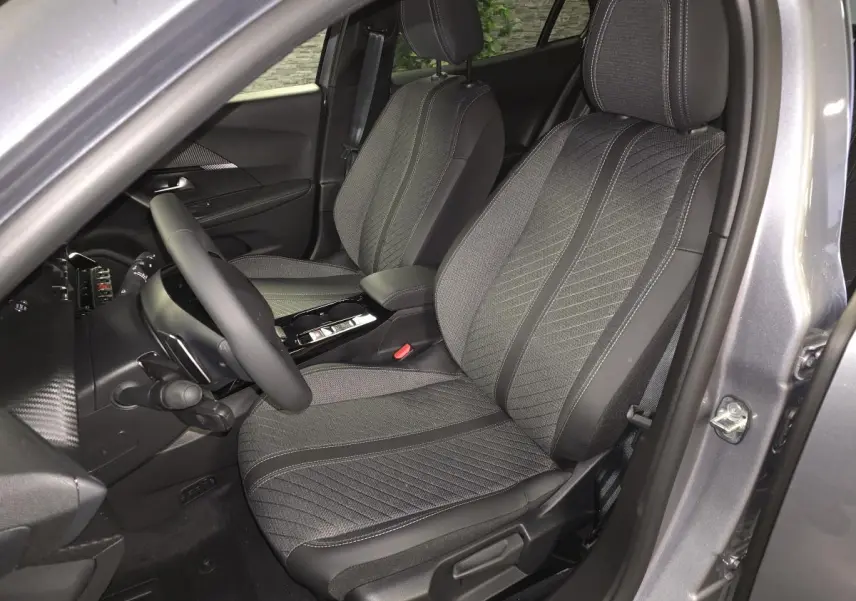 Vue intérieure côté conducteur de la Peugeot 2008 gris 2025, sièges tissu et TEP avec surpiqûres Quartz et volant cuir.