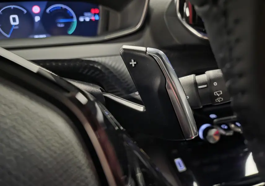 Gros plan sur la palette de changement de vitesse droite en chrome et noir dans l'habitacle du Peugeot 2008 gris hybride 2025.