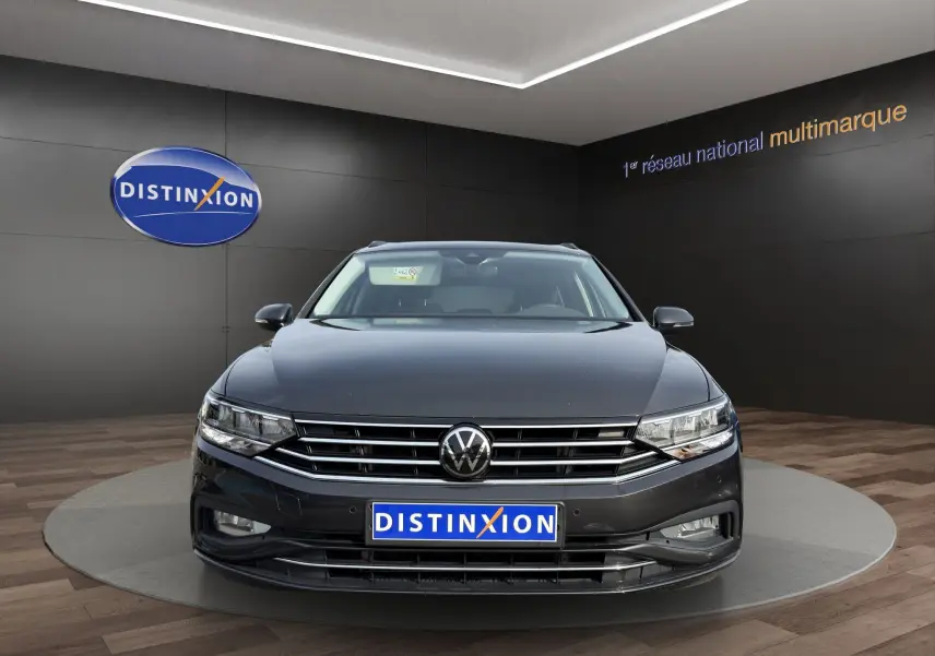 Vue frontale d'une Volkswagen Passat gris foncé, avec calandre chromée et phares LED, en showroom Distinxion.