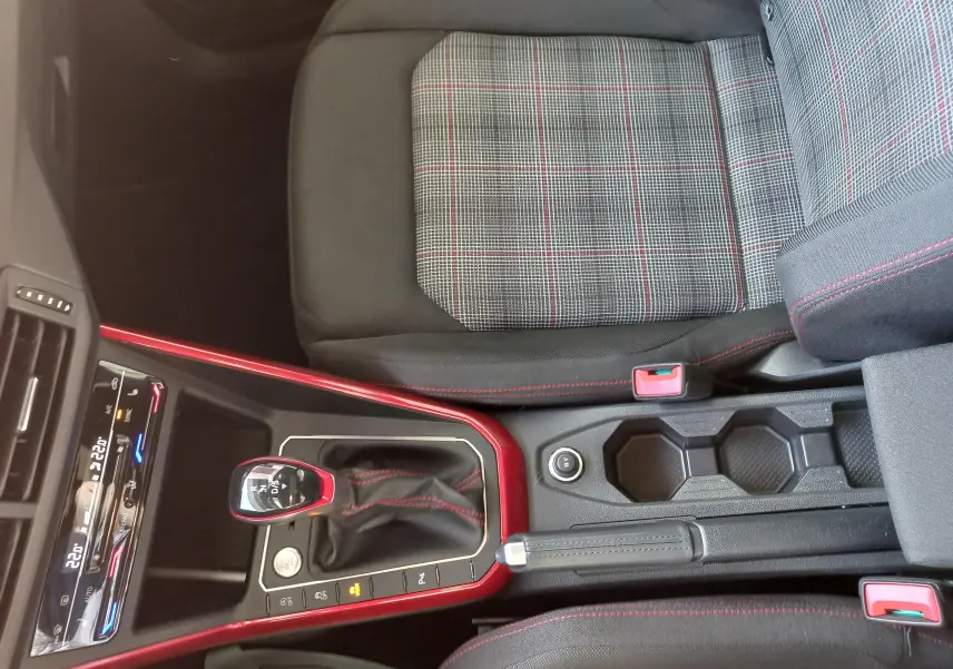 Vue intérieure centrée sur la console centrale et le levier de vitesse rouge et noir, siège tissu à motifs carreaux avec surpiqûres rouges.
