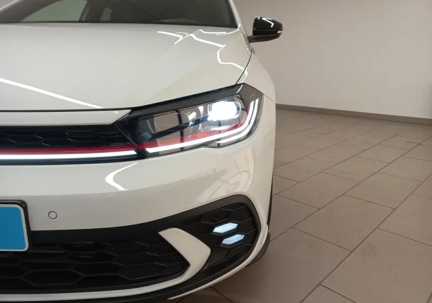 Gros plan sur l'avant droit blanc pur d'une Volkswagen Polo 2.0 TSI GTI 2024 avec phare LED et bandeau rouge distinctif.