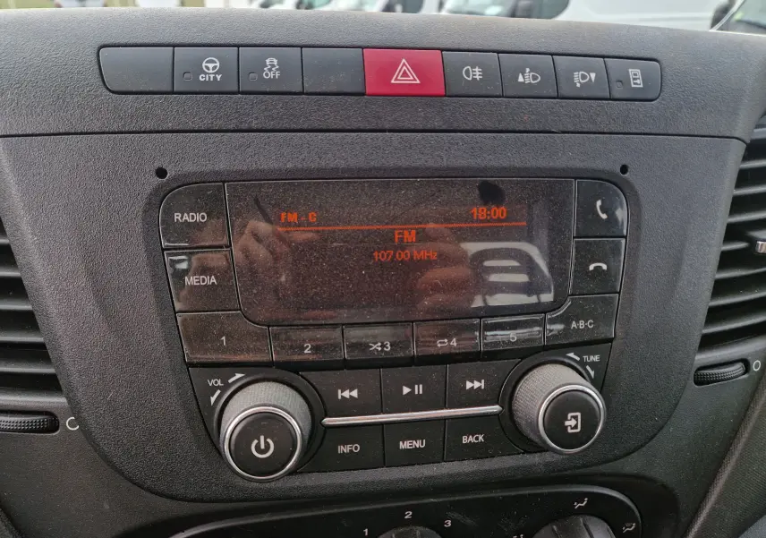 Vue rapprochée du tableau de bord noir de l'Iveco Daily 35C14 avec commandes radio et boutons d'alerte visibles.