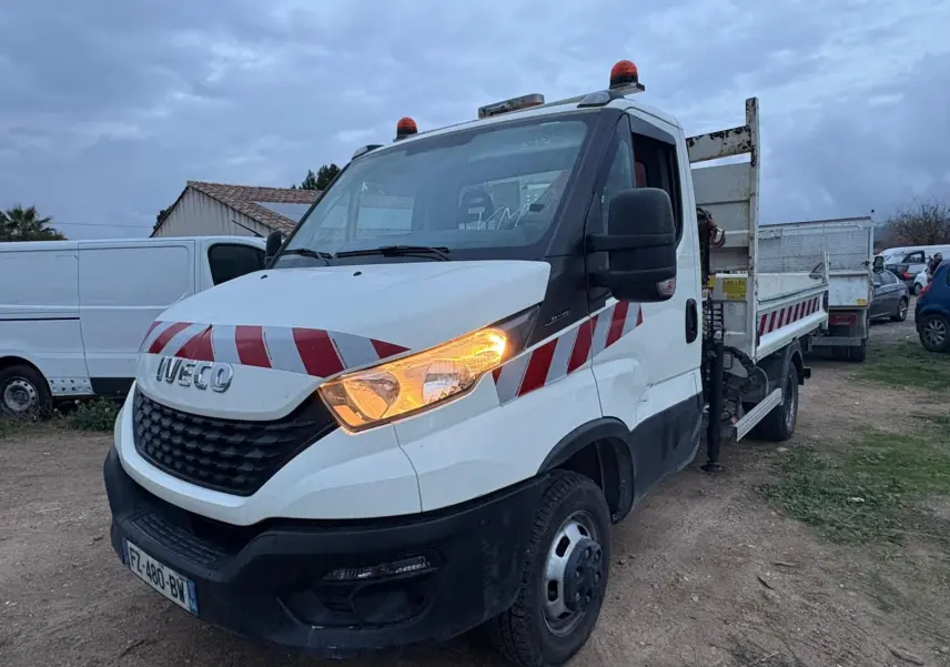 IVECO Daily 35C14 blanc en 3/4 avant droit, avec benne, grue Palfinger et feux allumés.