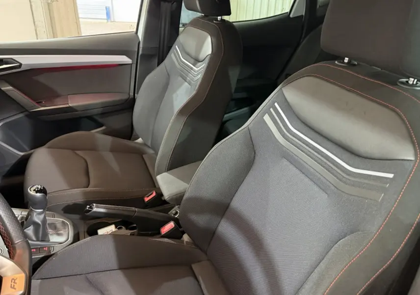 Vue intérieure côté conducteur de la SEAT Ibiza 1.0 TSI 110 FR 2024, sièges noirs avec surpiqûres rouges et levier de vitesses manuel.