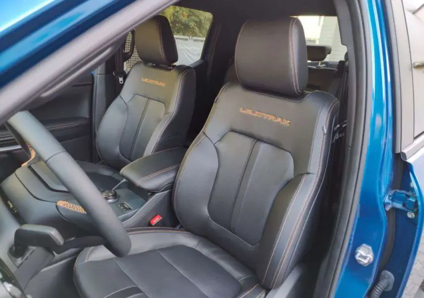 Vue intérieure côté conducteur du Ford Ranger Wildtrak bleu lightning, sièges cuir noirs avec surpiqûres orange et logo Wildtrak brodé.