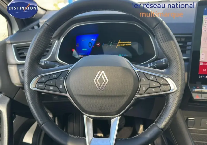 Vue intérieure centrée sur le volant noir perforé de la Renault Symbioz E-Tech 145 avec tableau de bord digital en arrière-plan.