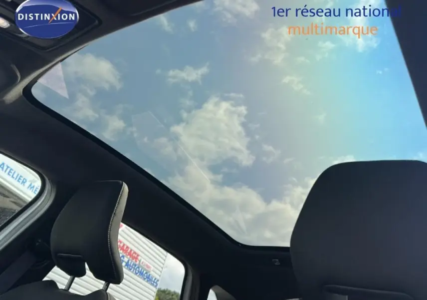 Vue intérieure du toit panoramique et des appuis-tête noirs du Renault Symbioz blanc, avec ciel nuageux visible.