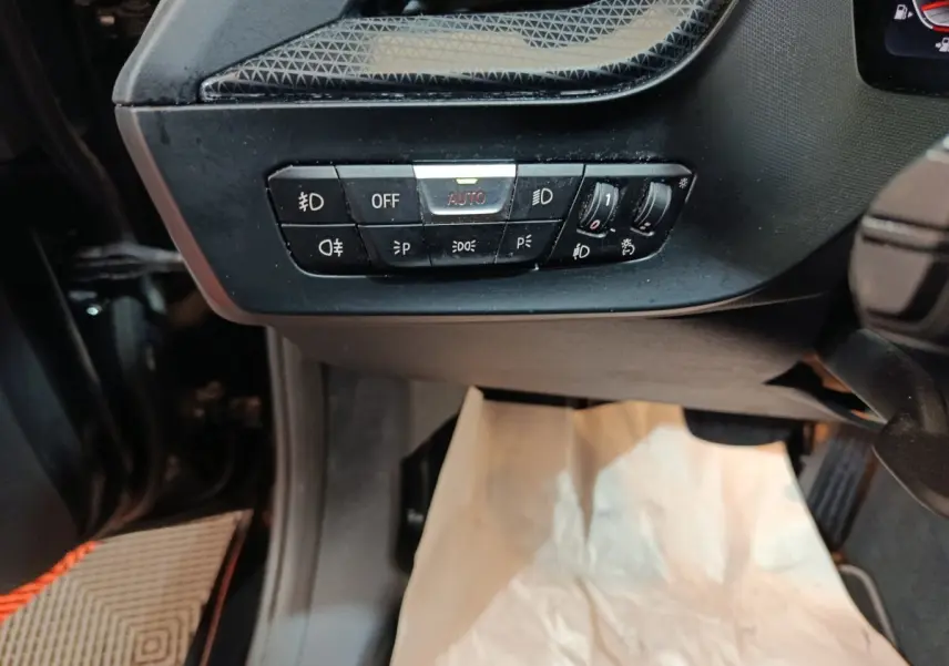 Vue rapprochée du tableau de bord côté gauche d’une BMW Série 1 noire, avec commandes d’éclairage et réglages lumineux.