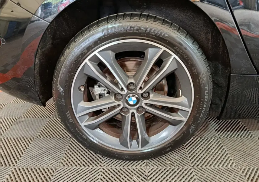 Gros plan sur la roue avant gauche noire d'une BMW Série 1 118i Edition Sport avec jante alliage gris foncé.