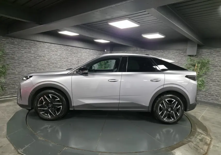 Vue de profil côté gauche d’un Peugeot 3008 gris métallisé 2025 avec jantes alliage noires et toit noir dans un showroom.