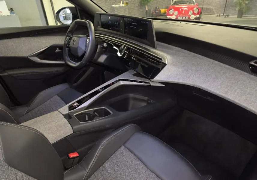 Intérieur de la Peugeot 3008 Hybrid 2025 vu côté passager, avec tableau de bord tissu gris et volant compact noir.