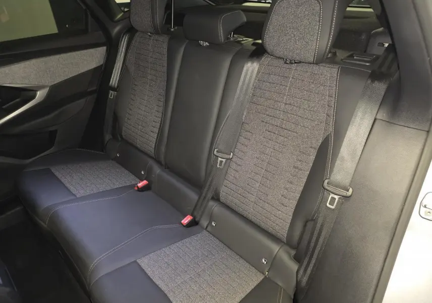 Vue latérale droite de la banquette arrière gris tissu et noir cuir du Peugeot 3008 2025 hybride avec ceintures de sécurité visibles.