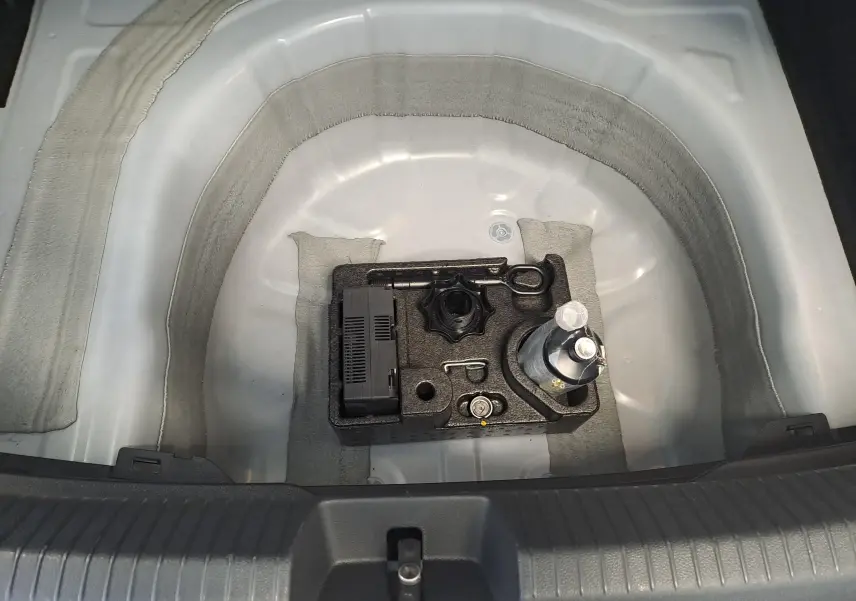 Coffre ouvert d'un Volkswagen Taigo blanc pur, vue plongeante sur le rangement d'outils et compresseur intégré.
