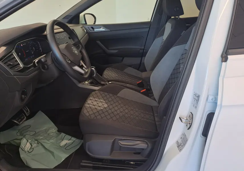 Vue intérieure côté conducteur du Volkswagen Taigo blanc pur 2025, sièges tissu noir et gris à motifs géométriques.
