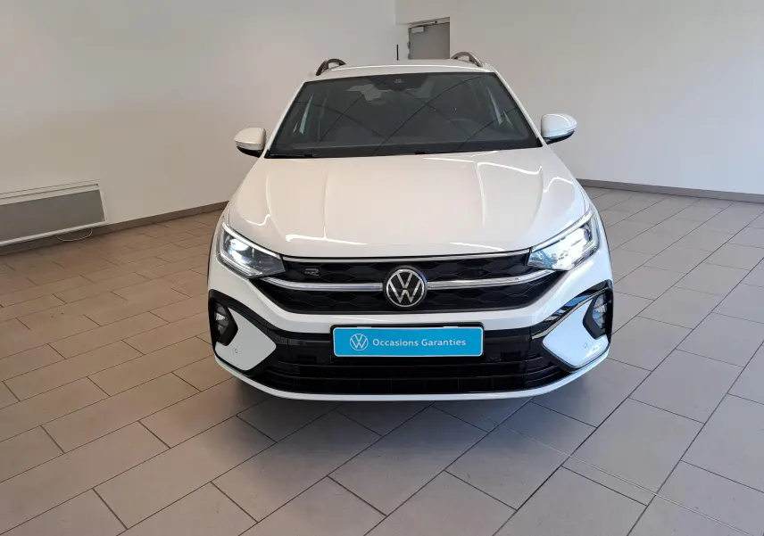 Vue avant d'un Volkswagen Taigo blanc pur 2025 avec calandre R-Line et phares allumés en intérieur showroom.