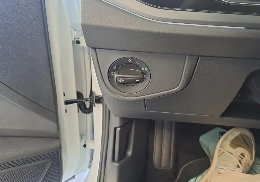 Vue intérieure côté gauche du tableau de bord du Volkswagen Taigo blanc, avec commande d'éclairage et partie de la portière ouverte.