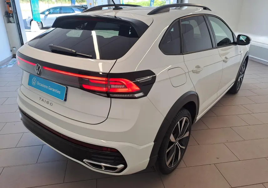Vue 3/4 arrière droite du Volkswagen Taigo blanc pur avec feux arrière allumés et jantes alliage 18 pouces Misano.