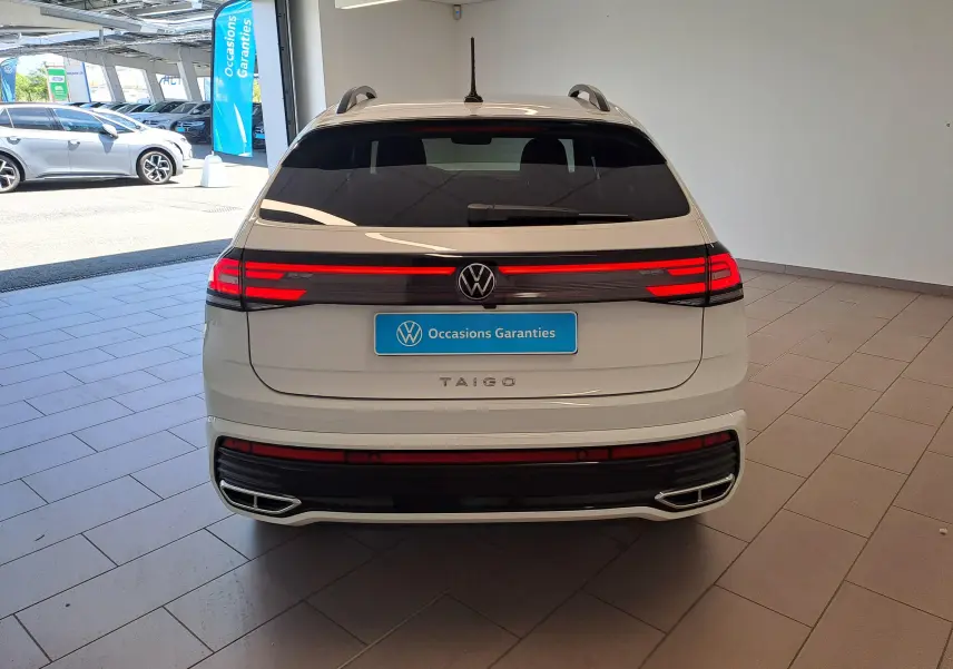 Vue arrière d'un Volkswagen Taigo blanc pur avec feux LED allumés et logo central dans un showroom.