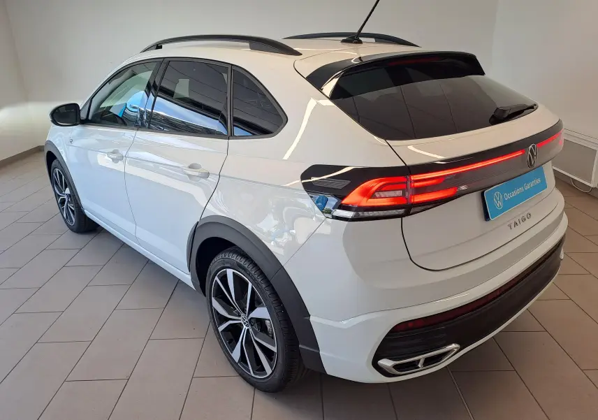 Vue 3/4 arrière droite du Volkswagen Taigo blanc pur avec jantes alliage 18 pouces et feux arrière LED allumés.