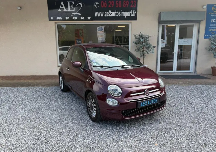 Fiat 500 violet vue 3/4 avant droit, berline compacte avec jantes alliage et calandre chromée devant un garage.