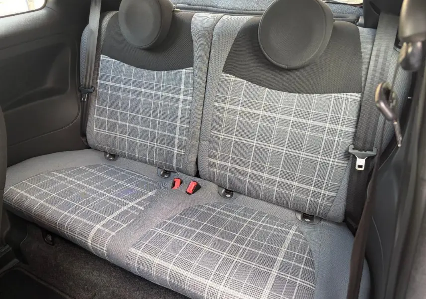Vue rapprochée des sièges arrière gris à motif carreaux d’une FIAT 500 berline violet, avec ceintures de sécurité visibles.