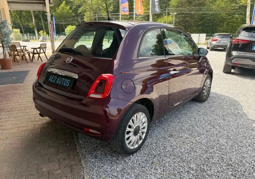 Vue 3/4 arrière droite d'une FIAT 500 berline violet foncé avec jantes alliage, stationnée sur un sol gravillonné.