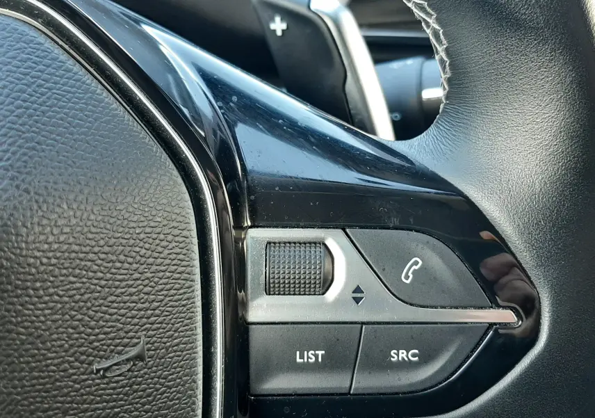 Gros plan sur les commandes gauche du volant noir du Peugeot 3008 gris Amazonite, avec molette et boutons d’appel.