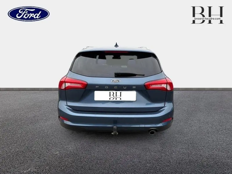 Vue arrière d'une Ford Focus SW 1.5 EcoBlue bleu azur métallisé avec attelage et feux arrière rouges.