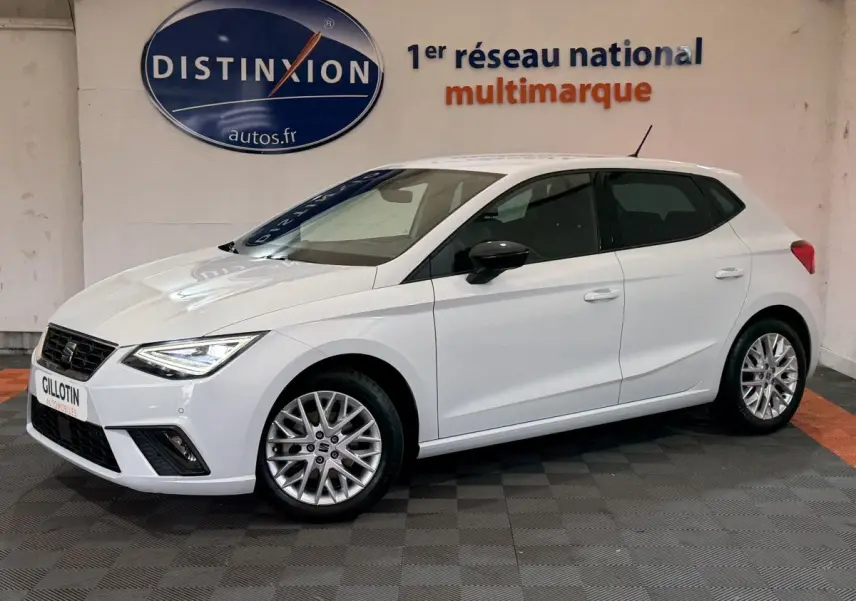 Vue 3/4 avant gauche d'une SEAT Ibiza 1.0 TSI 110 FR blanche avec jantes alliage et phares LED allumés.