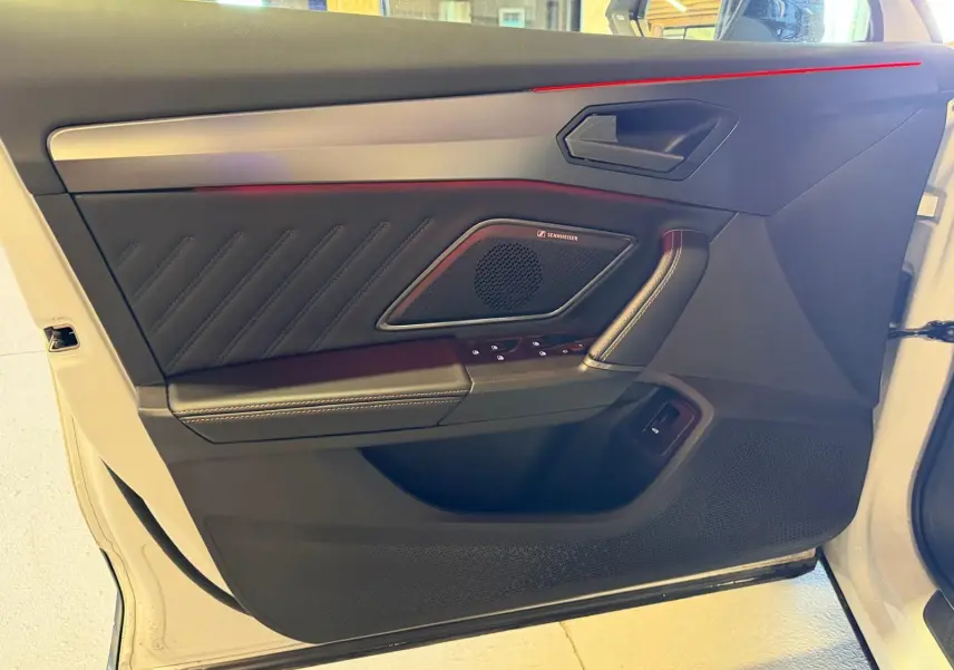 Vue intérieure côté porte avant gauche d'une CUPRA Formentor blanche, avec haut-parleur Sennheiser et éclairage d'ambiance rouge.