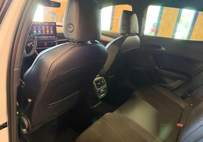 Vue intérieure arrière droite du CUPRA Formentor blanc 2025, sièges cuir noir et écran tactile avant visible.
