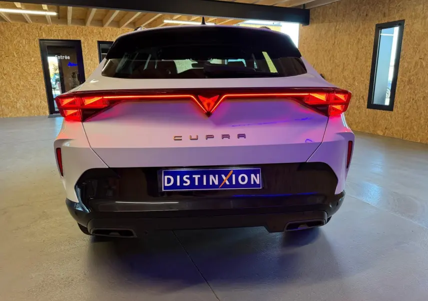 Vue arrière d'un CUPRA Formentor blanc 2025 avec feux LED allumés et logo lumineux dans un garage.