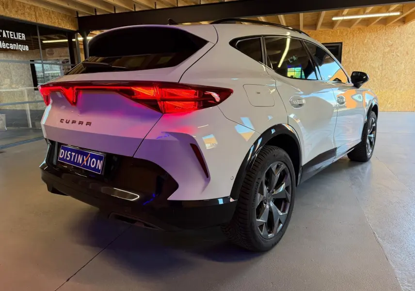 Vue 3/4 arrière droite du CUPRA Formentor blanc 2025 avec feux arrière LED et jantes foncées en intérieur d'atelier.