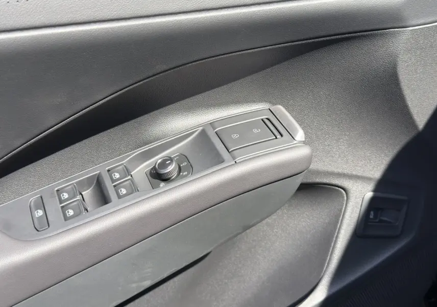 Gros plan sur la commande des vitres et rétroviseurs côté conducteur du Volkswagen T-Roc noir, intérieur moderne.