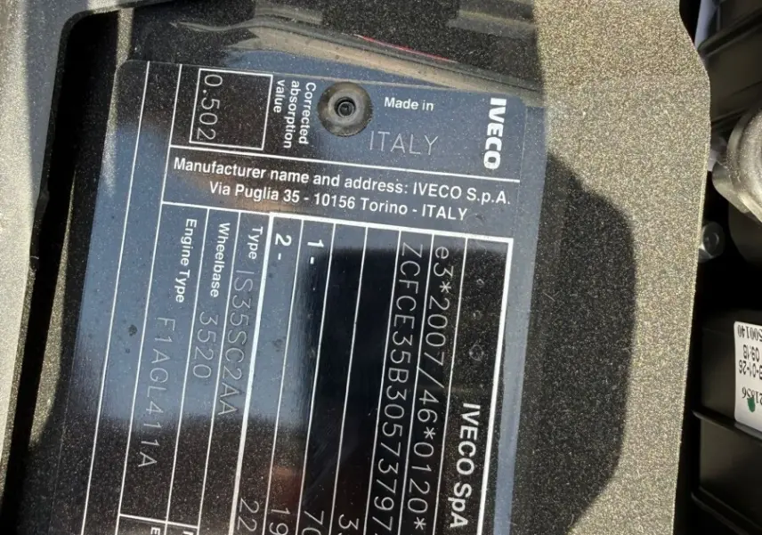 Gros plan sur la plaque constructeur noire du moteur d’un Iveco Daily blanc, montrant les détails techniques et l’origine Italie.