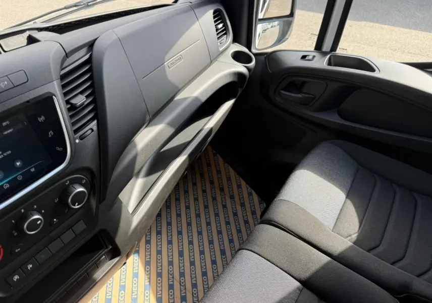 Vue intérieure côté passager du tableau de bord gris et siège tissu noir du fourgon Iveco Daily 2.3 blanc 2026.
