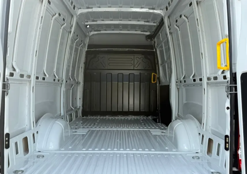 Vue intérieure arrière du fourgon Iveco Daily blanc 2026, montrant la grande zone de chargement vide avec poignées jaunes.