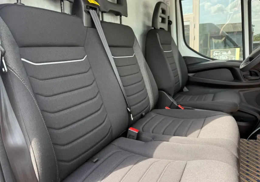 Vue intérieure côté passager montrant les sièges gris foncé du fourgon Iveco Daily 2026 avec ceinture de sécurité visible.