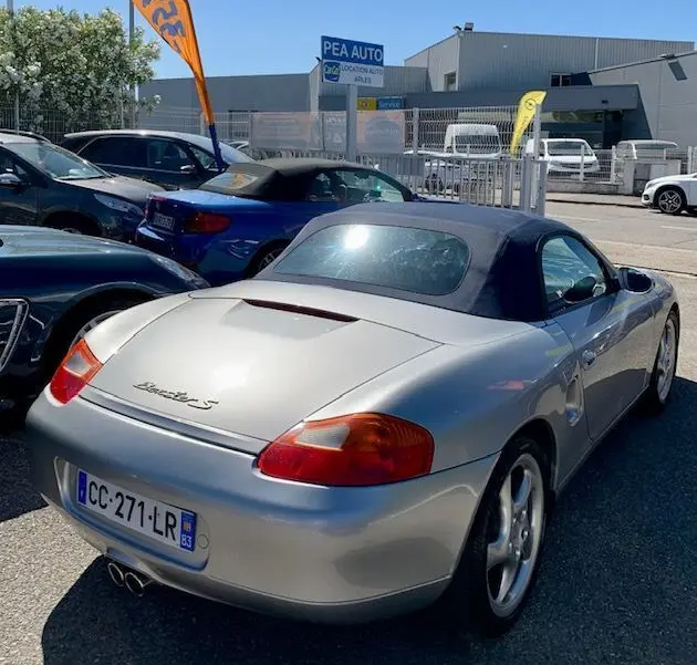 Vue 3/4 arrière droite d'une Porsche Boxster 986 gris métallisé de 2001 avec capote noire et double sortie d'échappement.