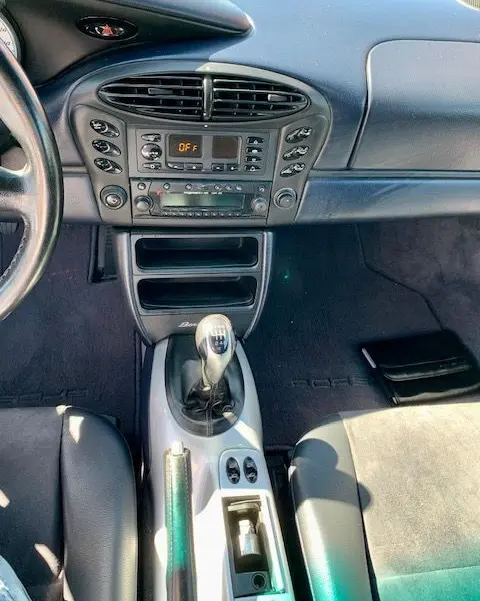 Vue intérieure centrée sur la console centrale et levier de vitesse manuelle d'une Porsche Boxster 986 gris de 2001.